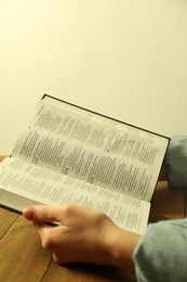 Woman reading Holy Bible in English language at wooden table, closeup