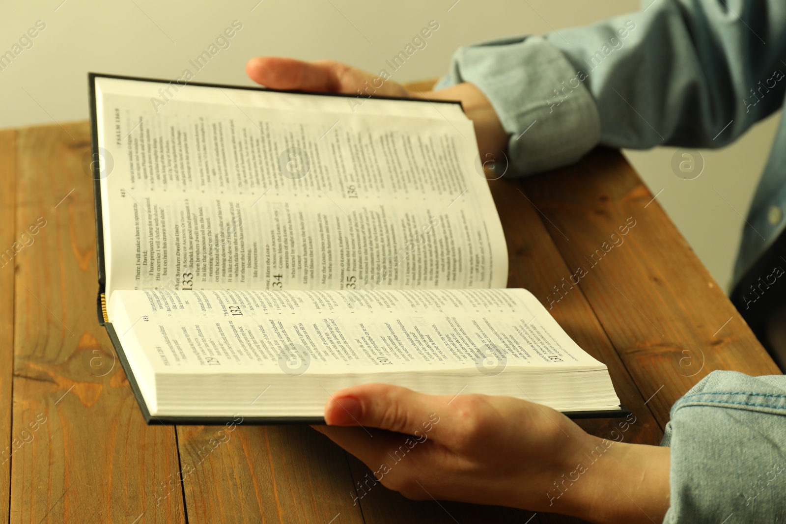 Photo of Woman reading Holy Bible in English language at wooden table, closeup