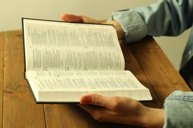 Woman reading Holy Bible in English language at wooden table, closeup