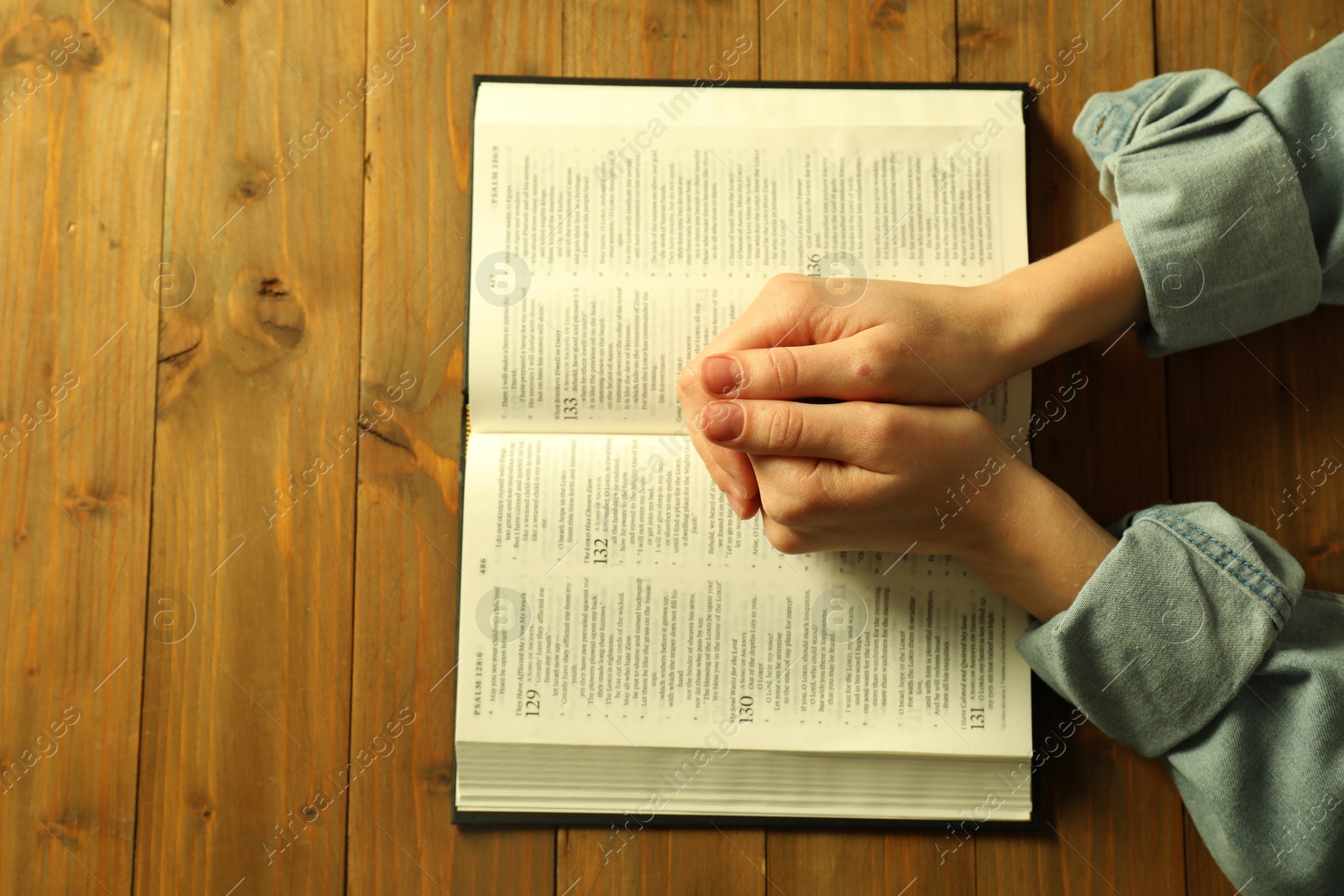 Photo of Woman with open Holy Bible in English language praying at wooden table, top view