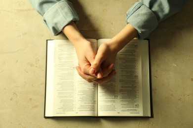 Photo of Woman with open Holy Bible in English language praying at beige table, top view