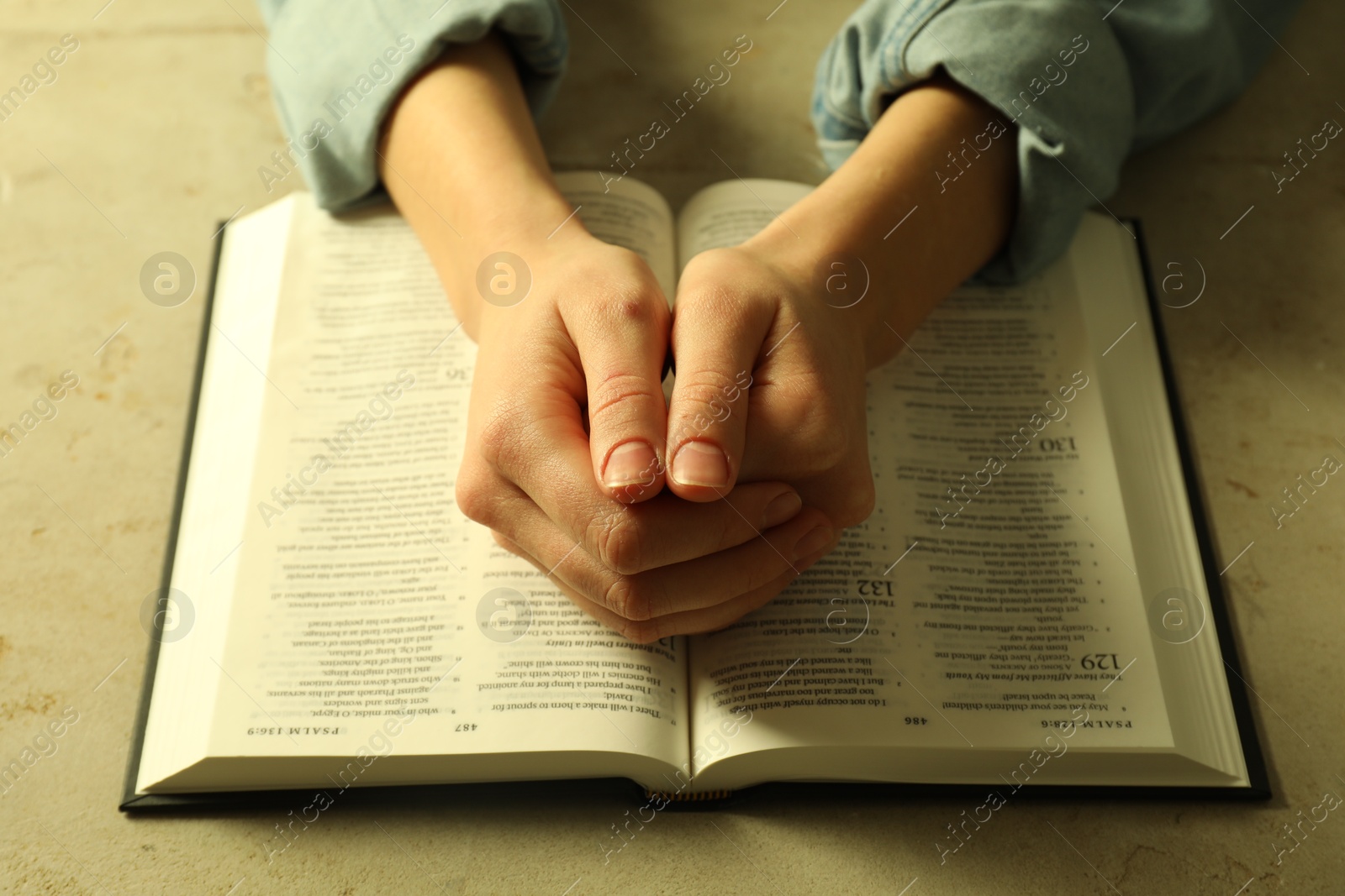 Photo of Woman with open Holy Bible in English language praying at beige table, closeup