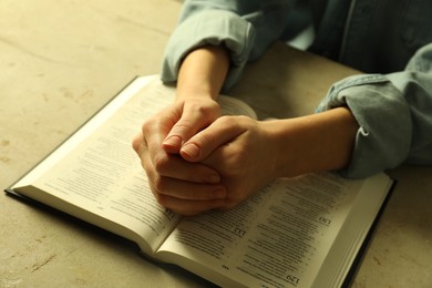 Photo of Woman with open Holy Bible in English language praying at beige table, closeup