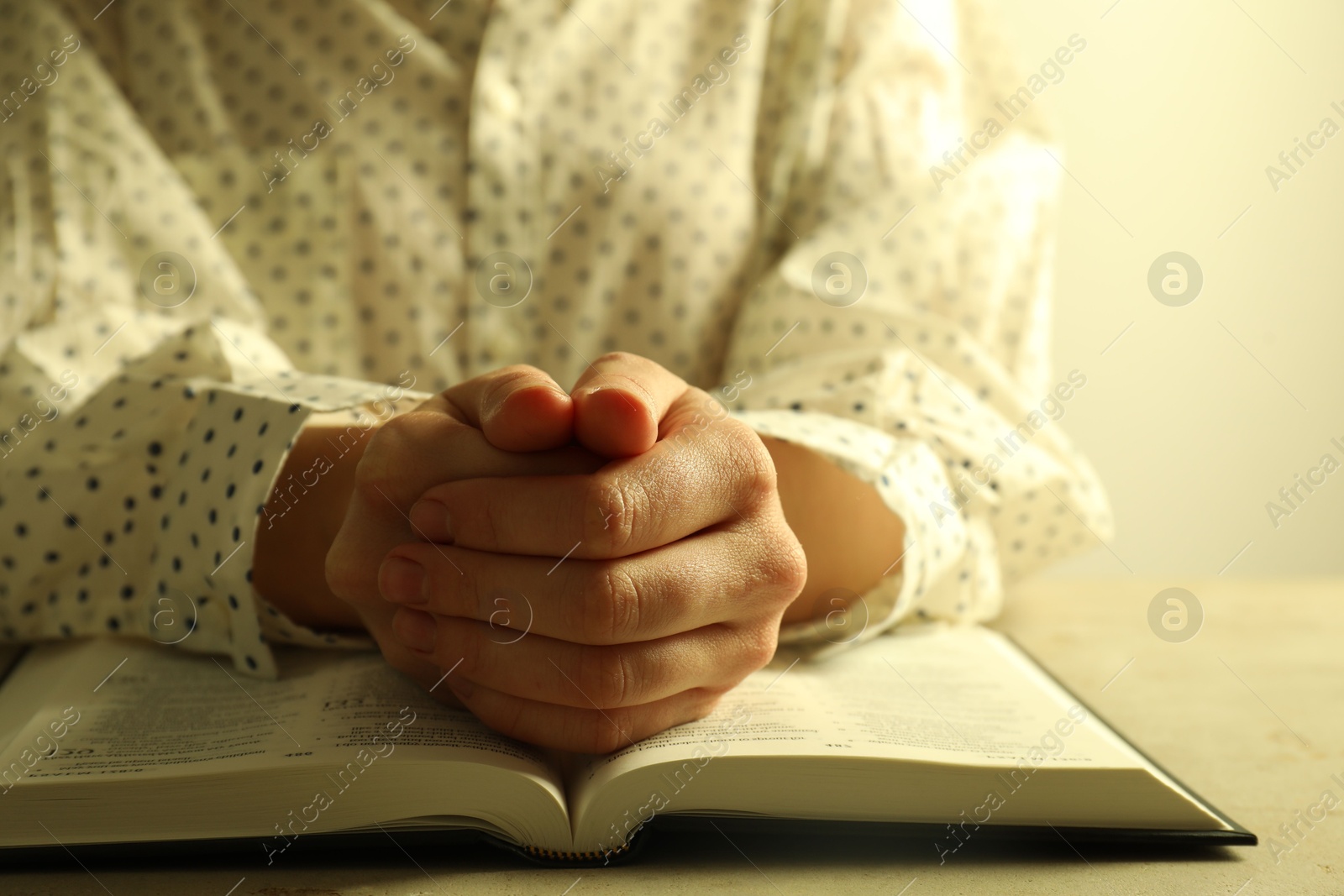 Photo of Woman with open Holy Bible in English language praying at beige table, closeup