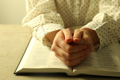 Woman with open Holy Bible in English language praying at beige table, closeup