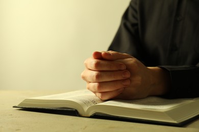 Photo of Woman with open Holy Bible in English language praying at beige table, closeup