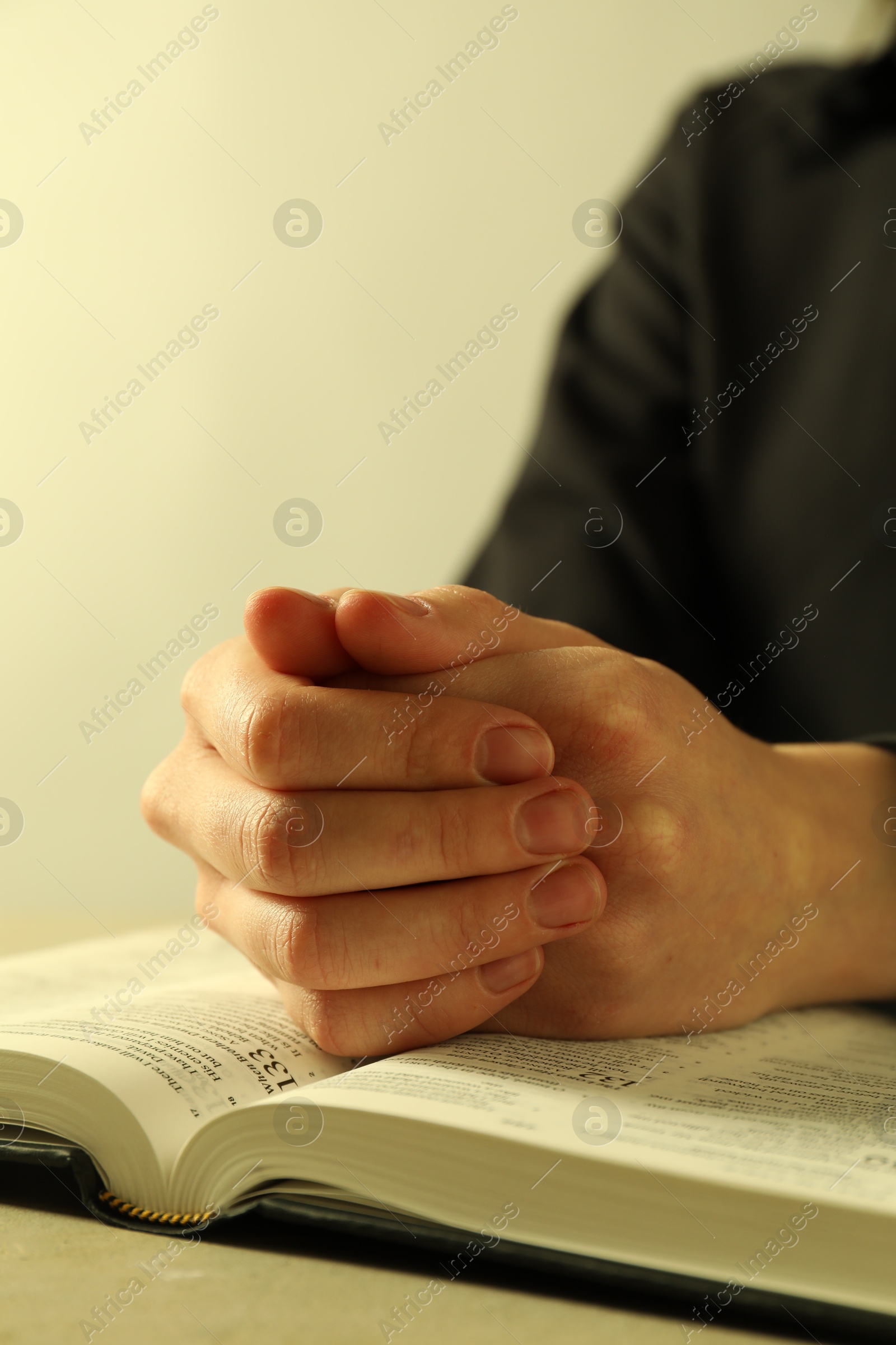 Photo of Woman with open Holy Bible in English language praying at beige table, closeup