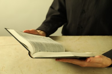 Woman reading Holy Bible in English language at beige table, closeup