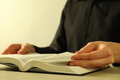 Woman reading Holy Bible in English language at beige table, closeup