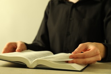 Woman reading Holy Bible in English language at beige table, closeup