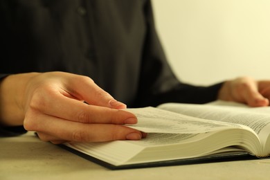 Photo of Woman reading Holy Bible in English language at beige table, closeup