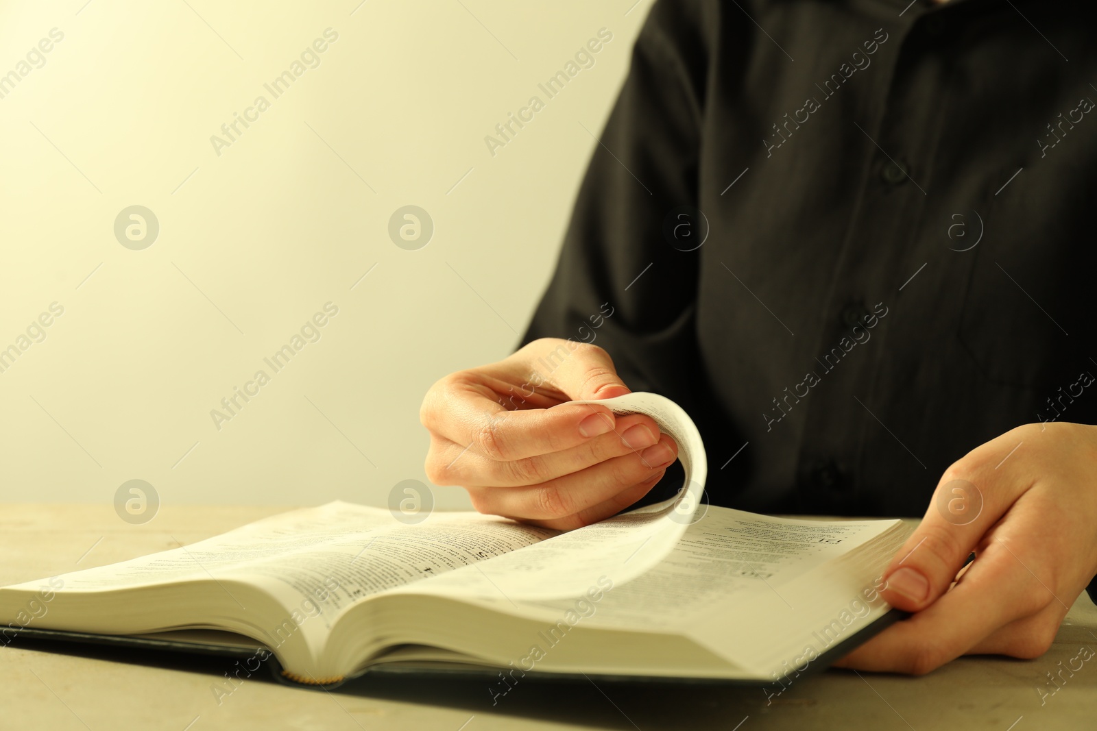 Photo of Woman reading Holy Bible in English language at beige table, closeup