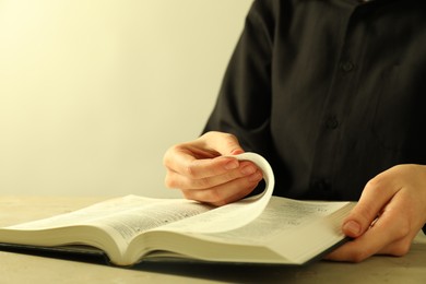 Woman reading Holy Bible in English language at beige table, closeup