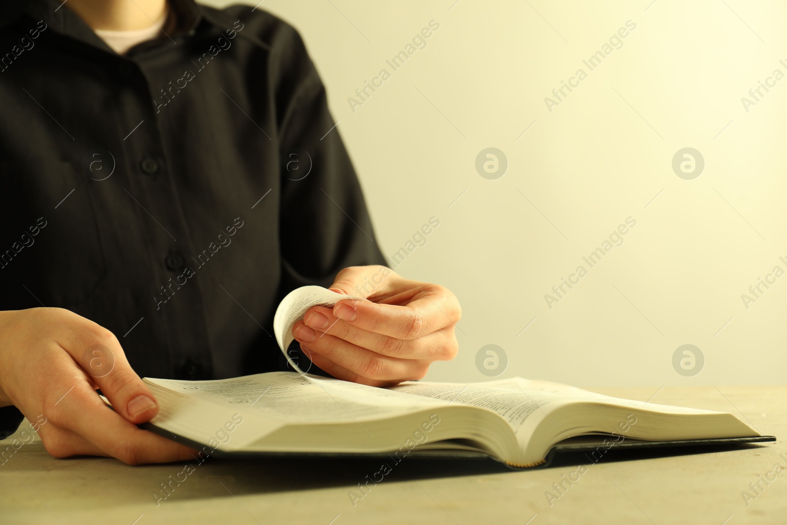 Photo of Woman reading Holy Bible in English language at beige table, closeup