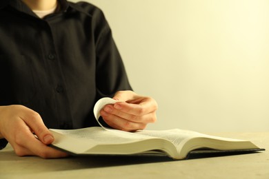 Woman reading Holy Bible in English language at beige table, closeup