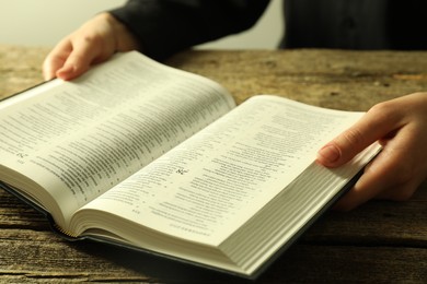 Photo of Woman with Holy Bible in English language at wooden table, closeup