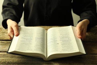 Photo of Woman with Holy Bible in English language at wooden table, closeup