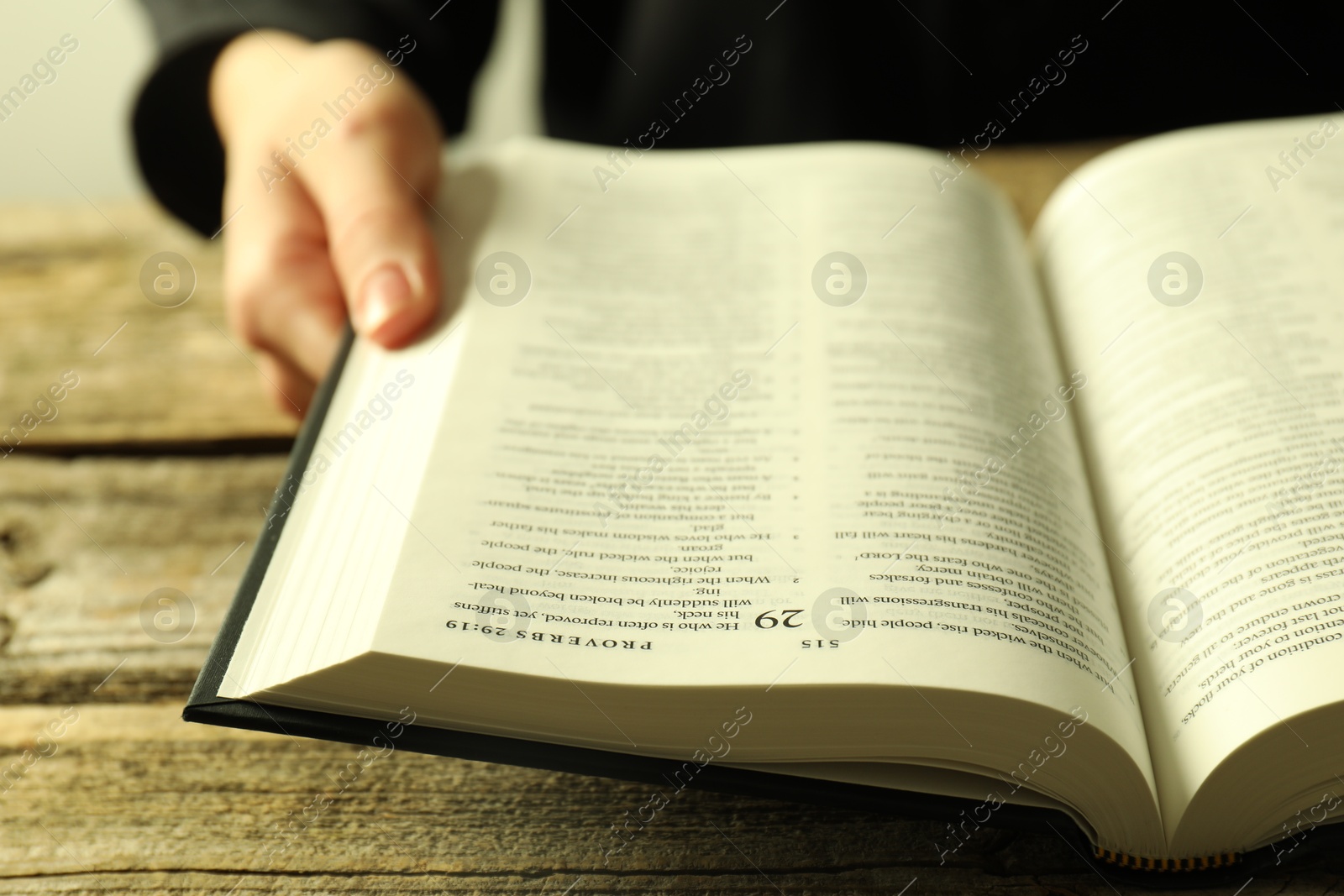 Photo of Woman with Holy Bible in English language at wooden table, closeup