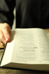 Photo of Woman reading Holy Bible in English language at wooden table, closeup