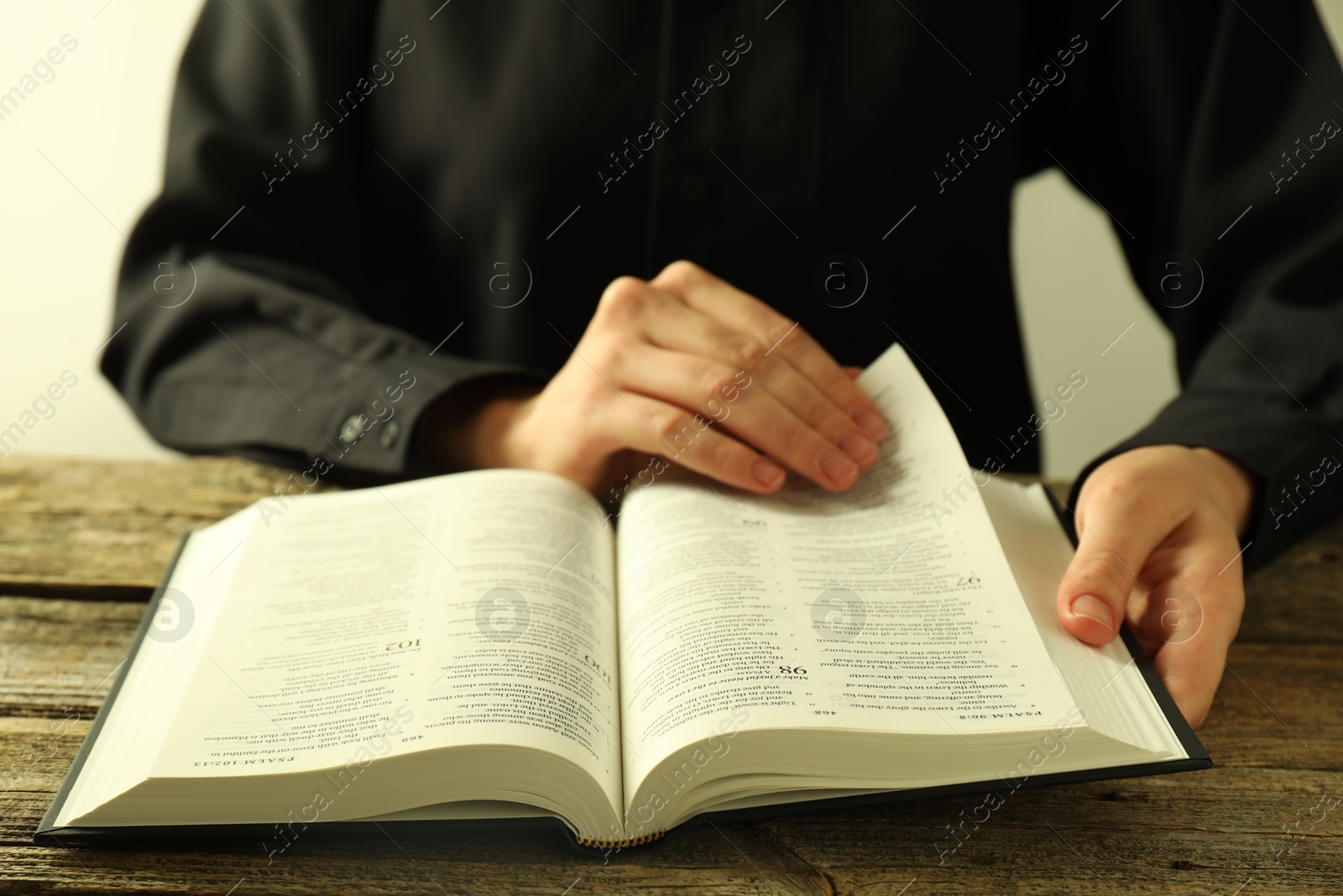 Photo of Woman reading Holy Bible in English language at wooden table, closeup