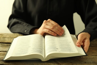 Woman reading Holy Bible in English language at wooden table, closeup