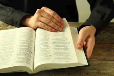 Woman reading Holy Bible in English language at wooden table, closeup