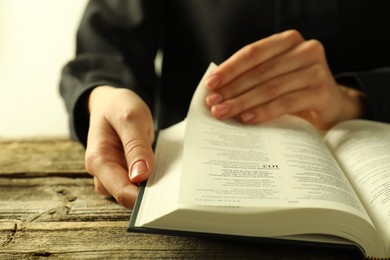 Photo of Woman reading Holy Bible in English language at wooden table, closeup