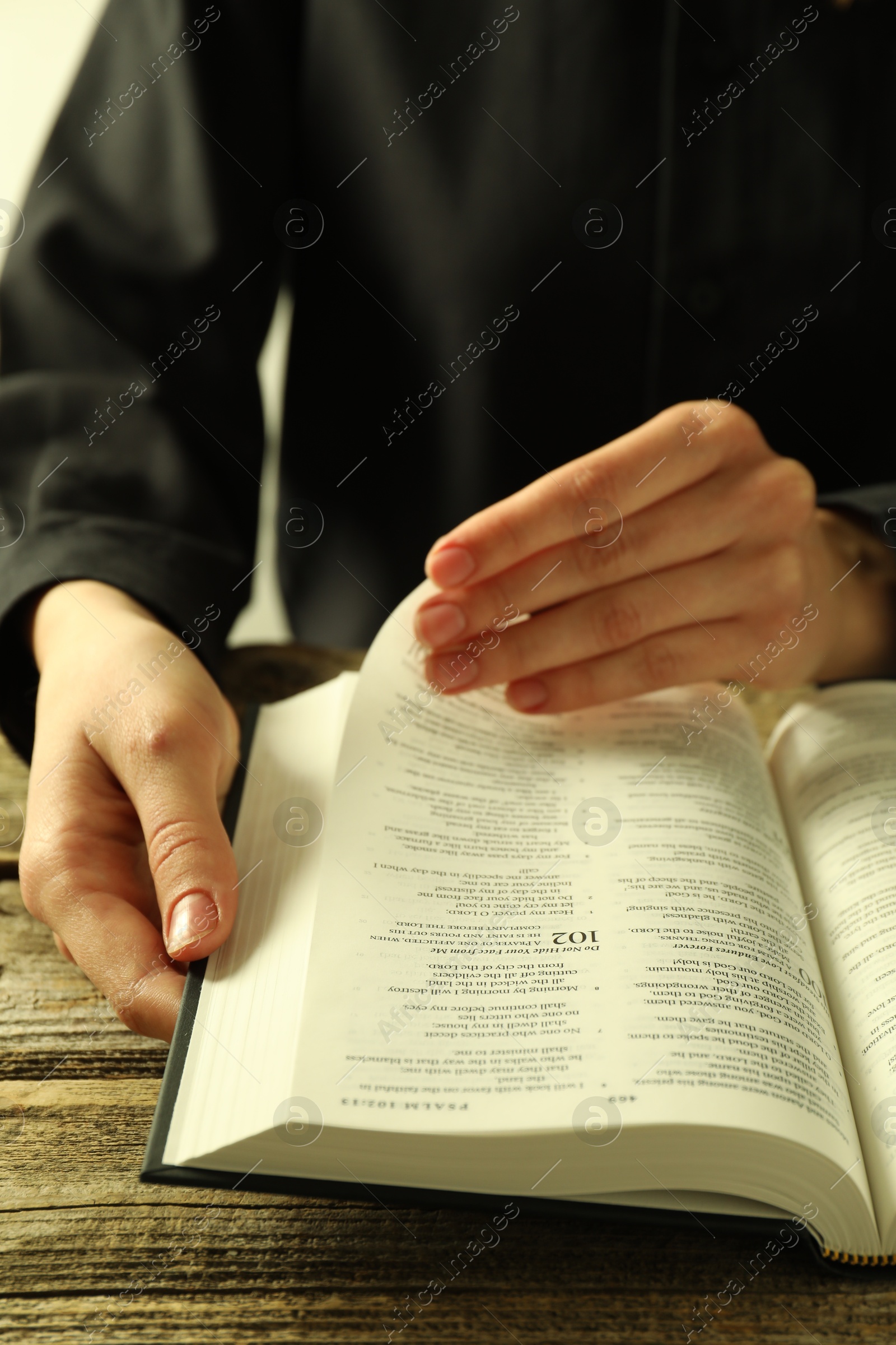 Photo of Woman reading Holy Bible in English language at wooden table, closeup