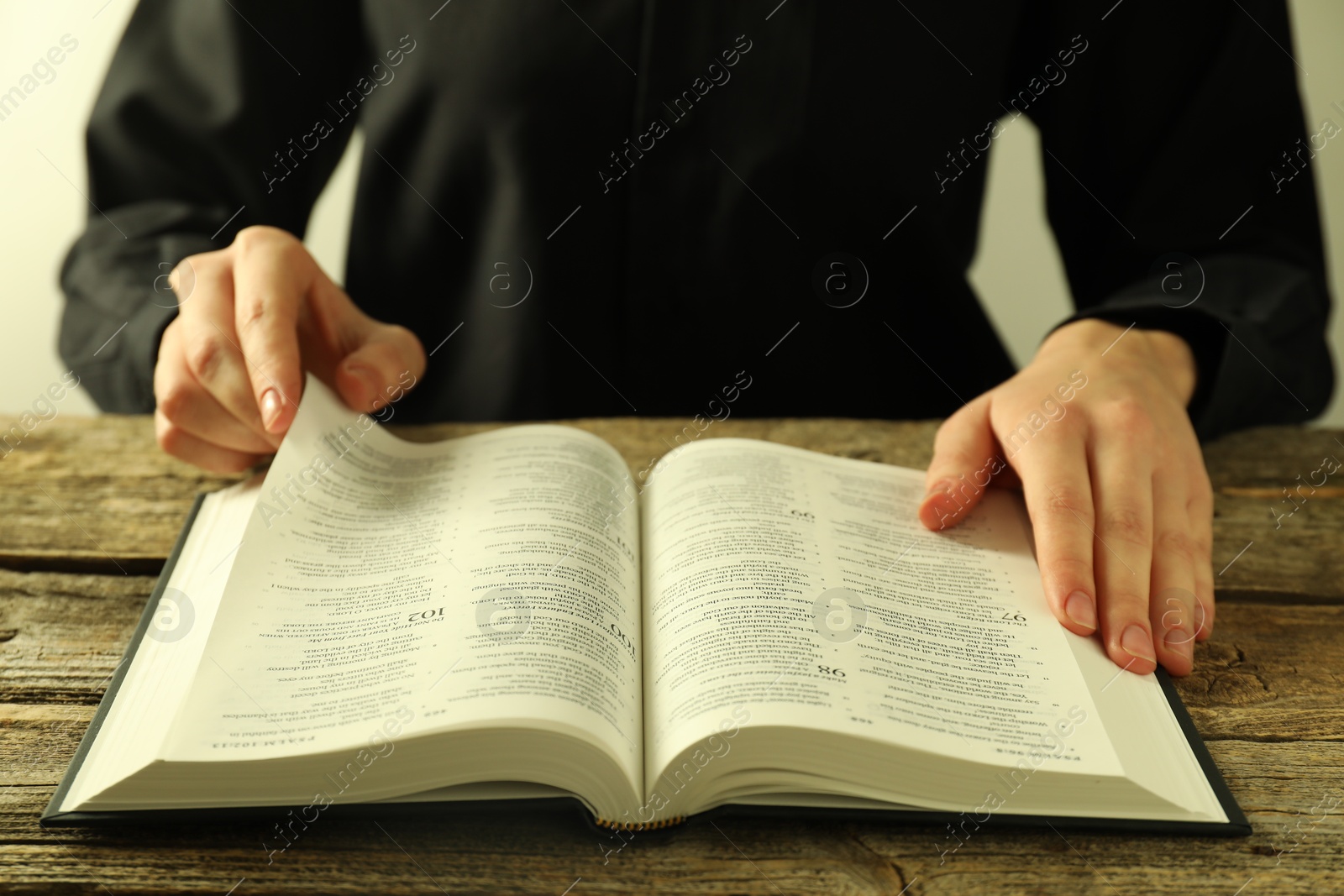 Photo of Woman reading Holy Bible in English language at wooden table, closeup