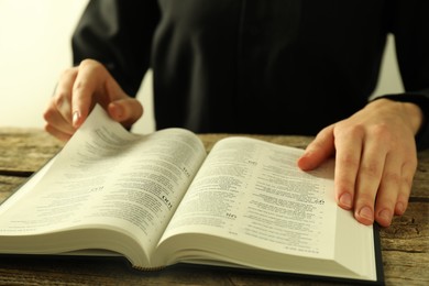 Woman reading Holy Bible in English language at wooden table, closeup