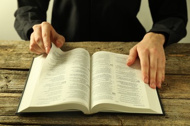 Photo of Woman reading Holy Bible in English language at wooden table, closeup