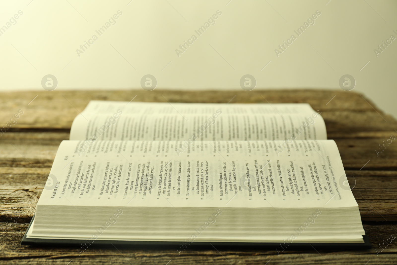 Photo of Open Holy Bible in English language on wooden table, closeup