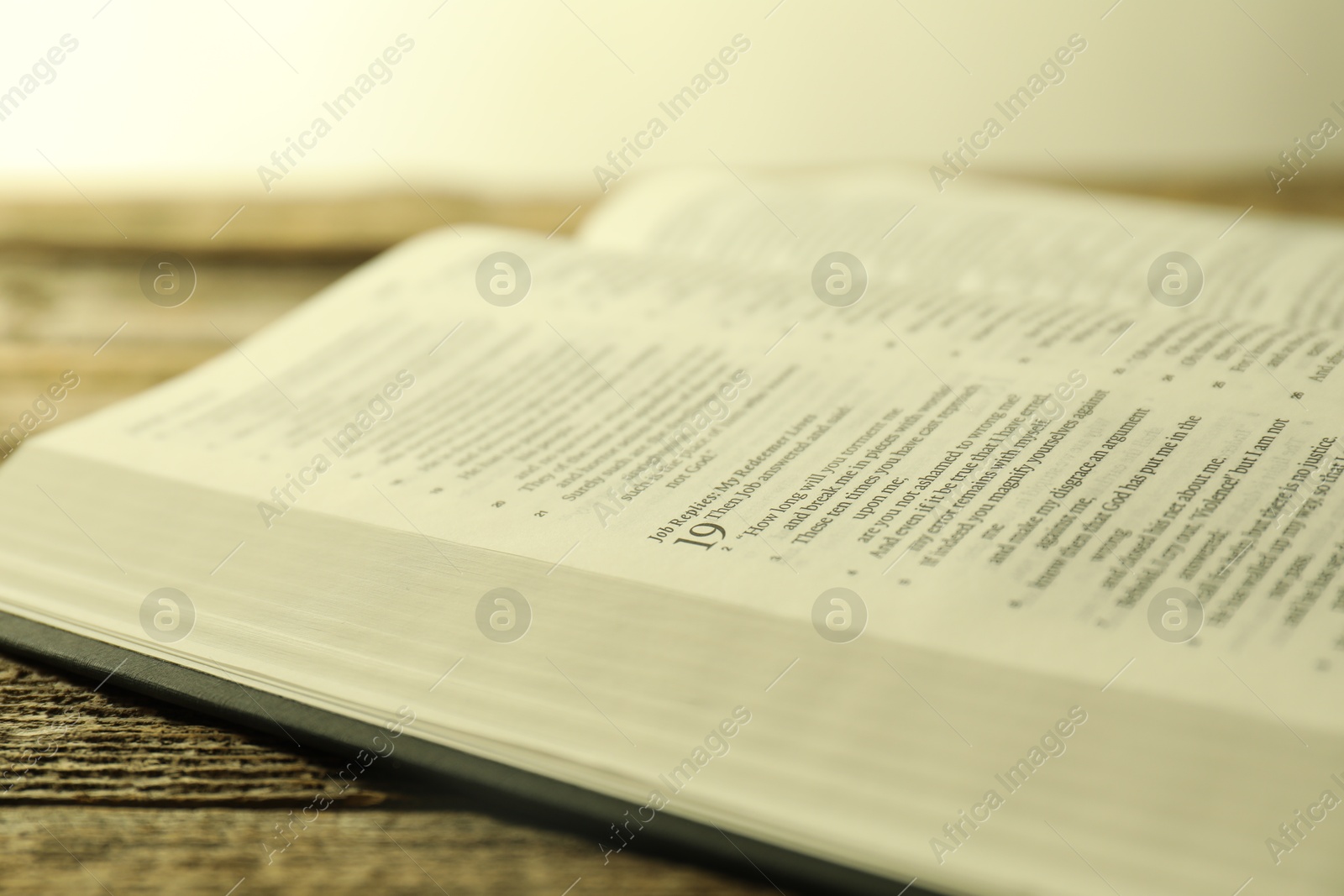 Photo of Open Holy Bible in English language on wooden table, closeup