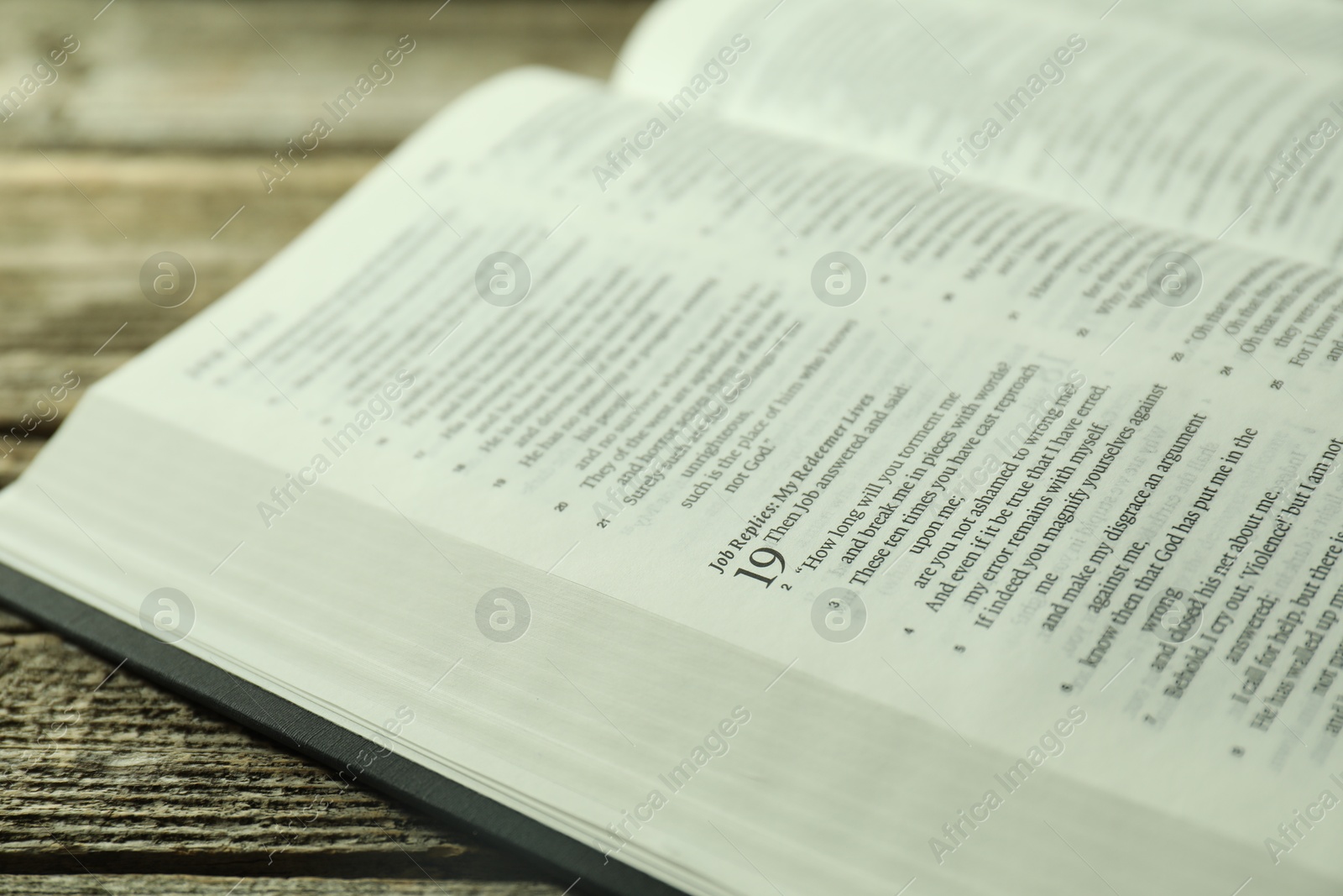 Photo of Open Holy Bible in English language on wooden table, closeup