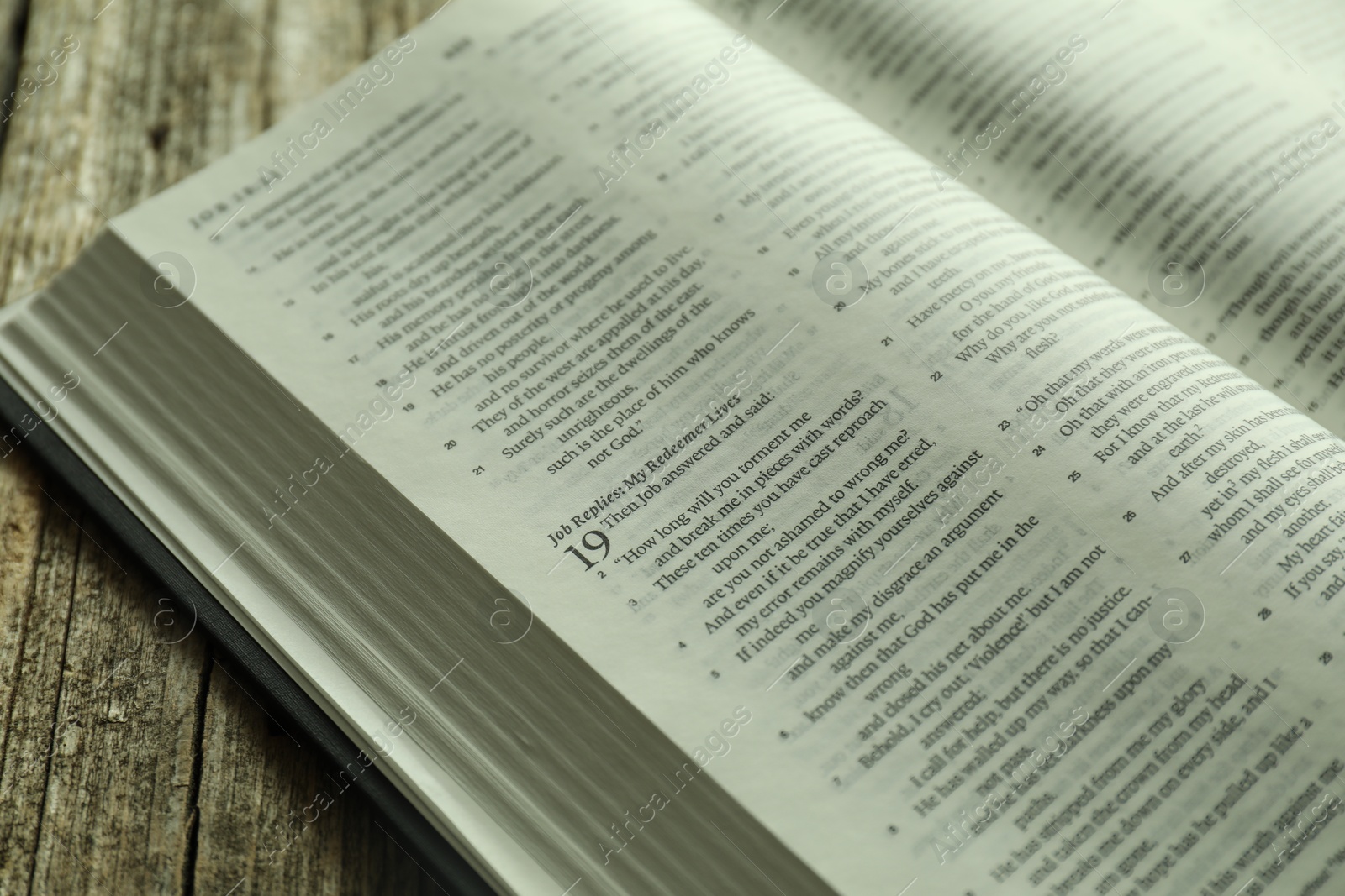 Photo of Open Holy Bible in English language on wooden table, closeup