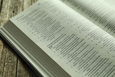 Photo of Open Holy Bible in English language on wooden table, closeup