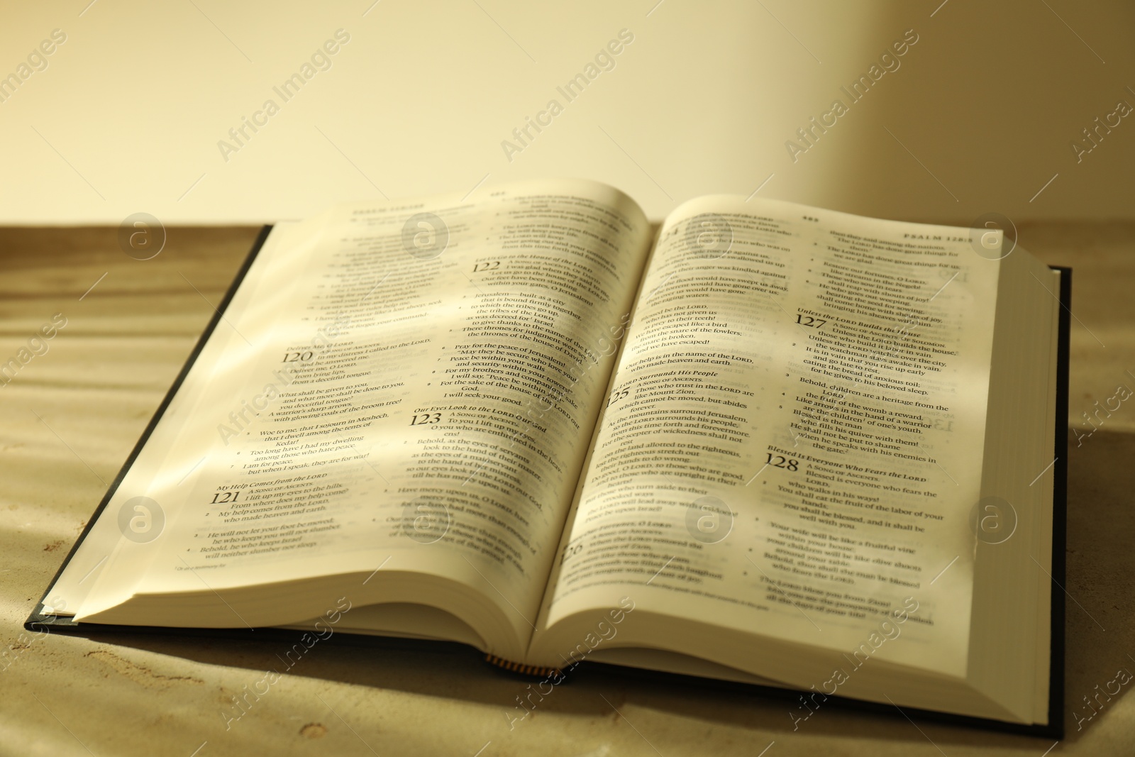 Photo of Open Holy Bible in English language on beige table, closeup