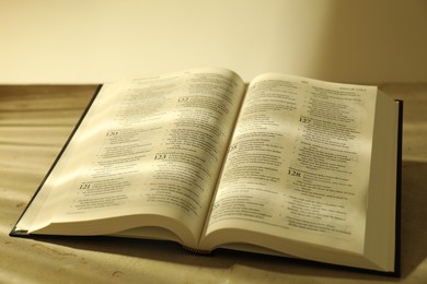 Photo of Open Holy Bible in English language on beige table, closeup