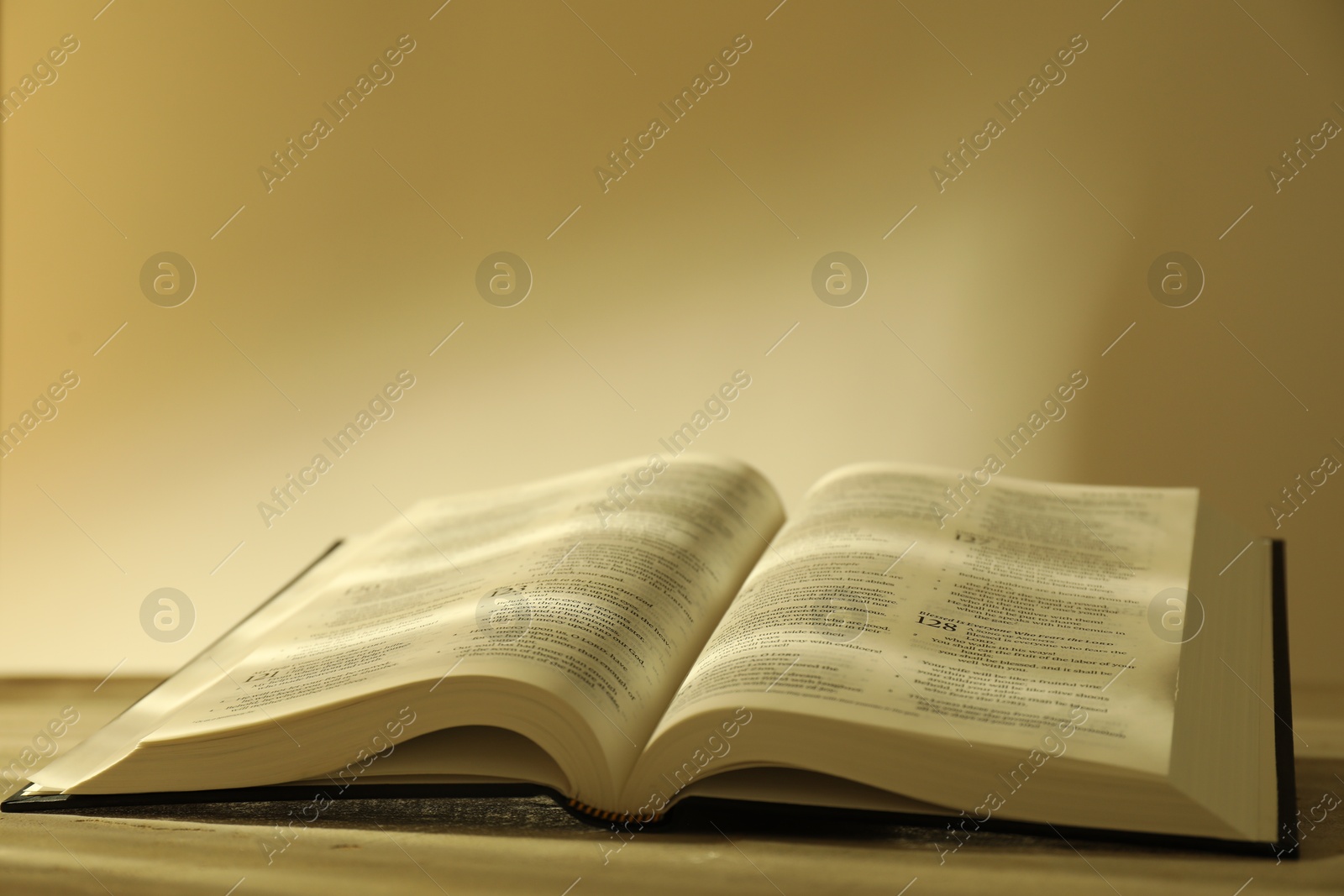 Photo of Open Holy Bible in English language on beige table, closeup