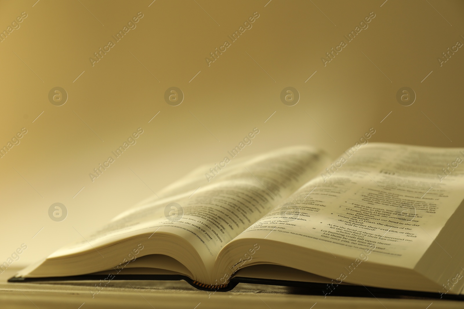 Photo of Open Holy Bible in English language on beige table, closeup