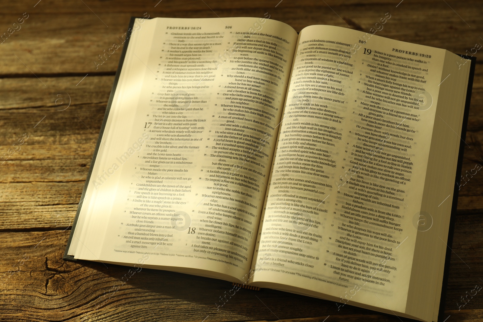 Photo of Open Holy Bible in English language on wooden table