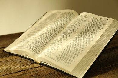 Photo of Open Holy Bible in English language on wooden table, closeup