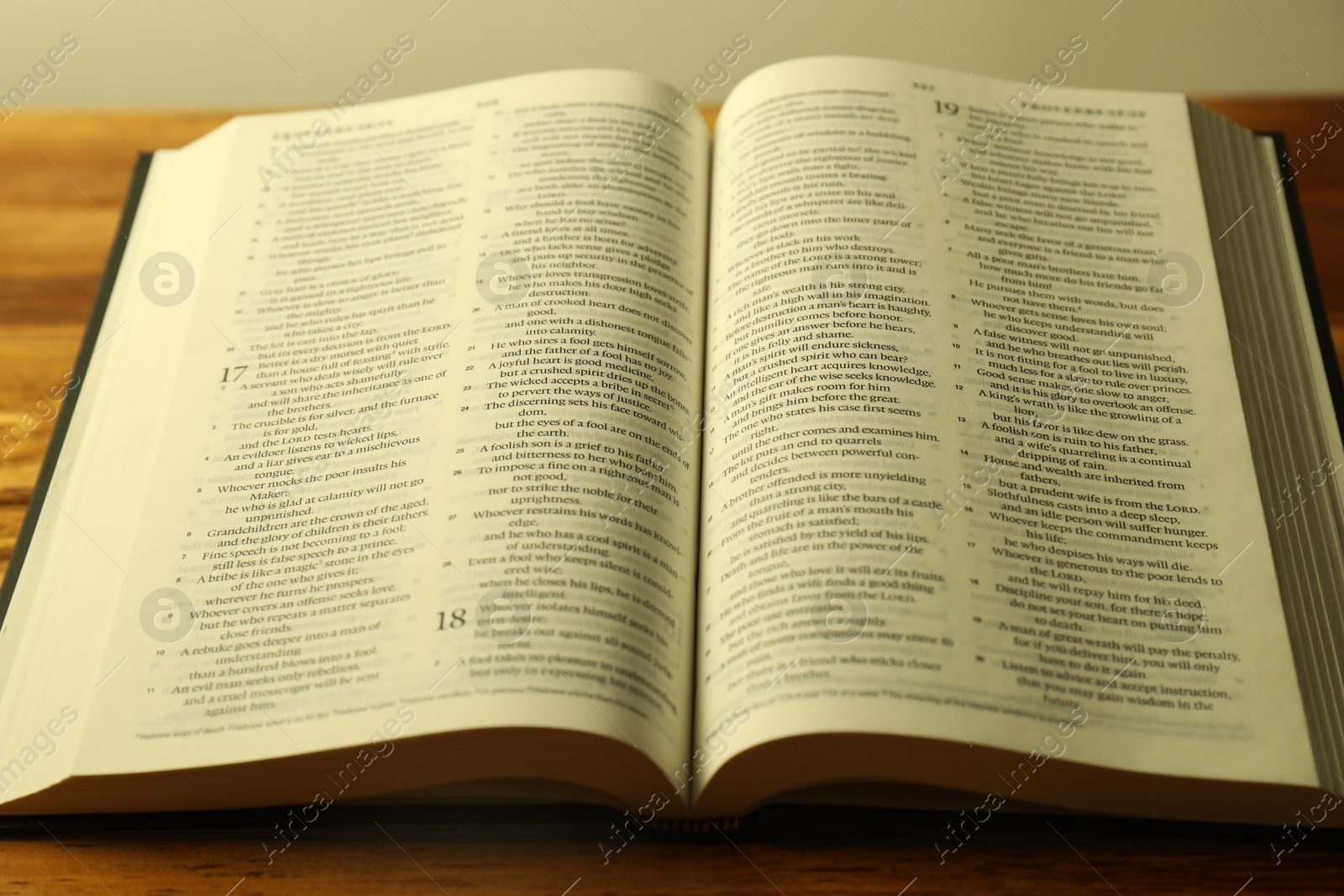 Photo of Open Holy Bible in English language on wooden table, closeup