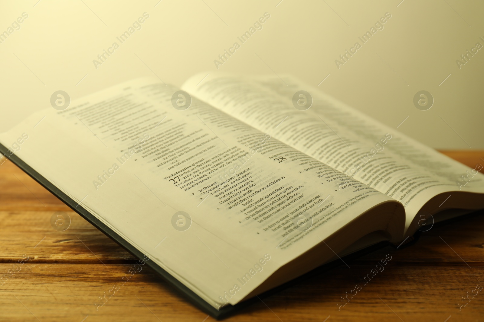 Photo of Open Holy Bible in English language on wooden table, closeup