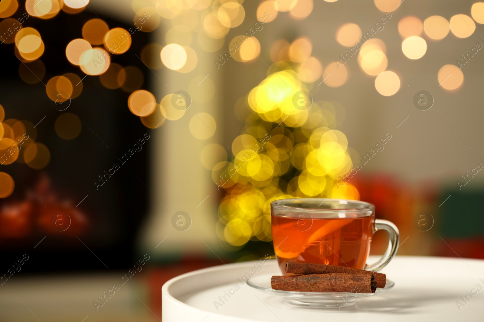 Photo of Cup of tea with lemon and cinnamon sticks on table against blurred Christmas lights, bokeh effect. Space for text