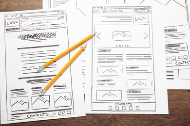 Photo of Developing UI design. Sketches of website wireframes and pencils on wooden table, top view