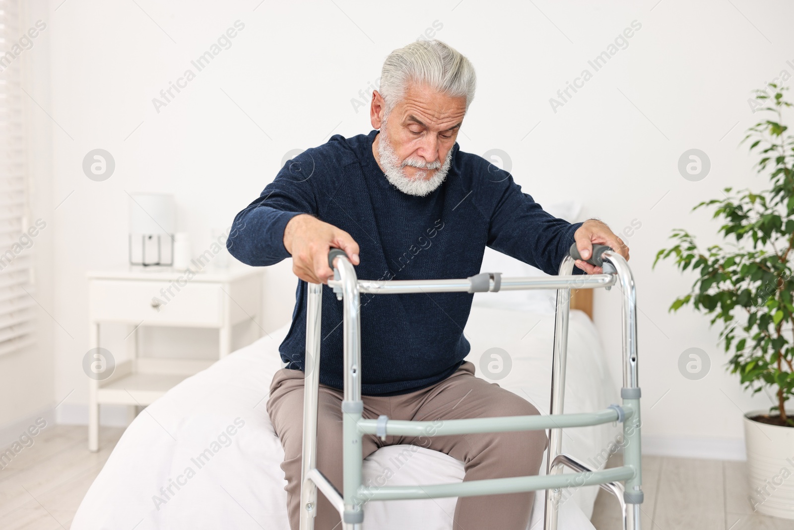 Photo of Senior man with walking frame on bed in hospital ward