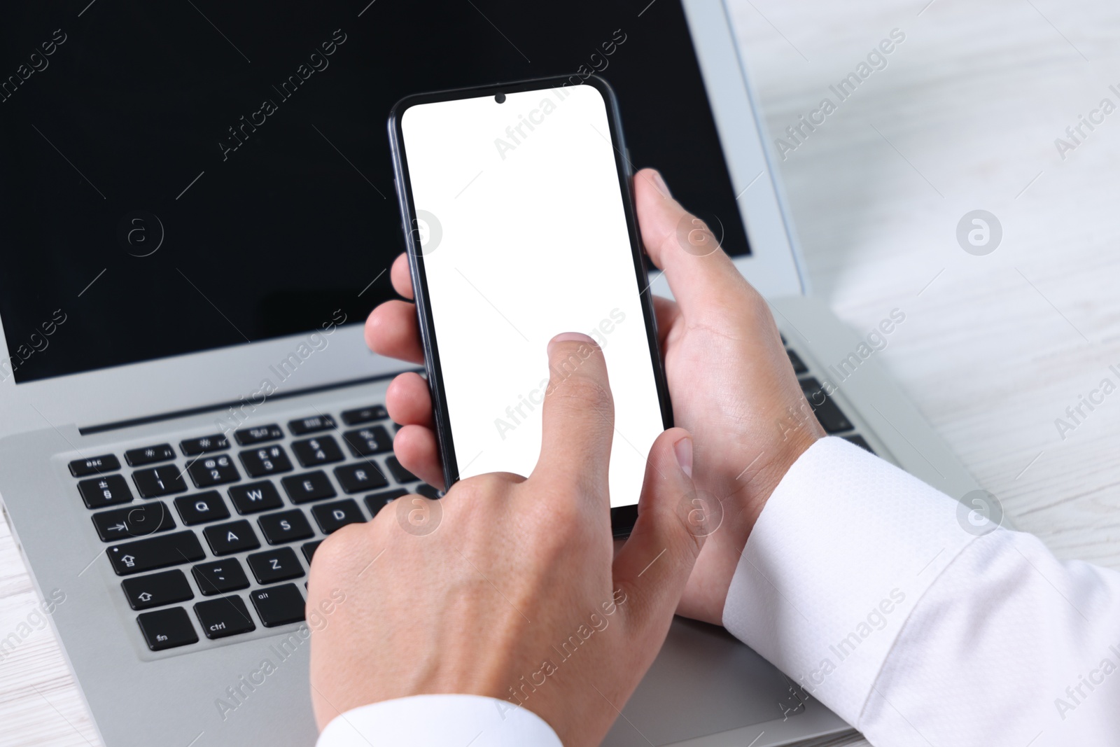 Photo of Man unlocking smartphone with fingerprint scanner near laptop at light wooden table, closeup