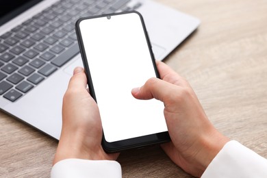 Photo of Woman unlocking smartphone with fingerprint scanner near laptop at wooden table, closeup