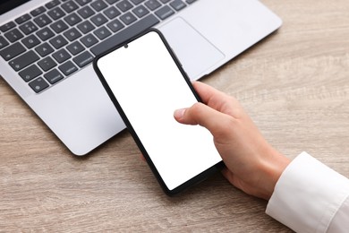 Photo of Woman unlocking smartphone with fingerprint scanner near laptop at wooden table, closeup